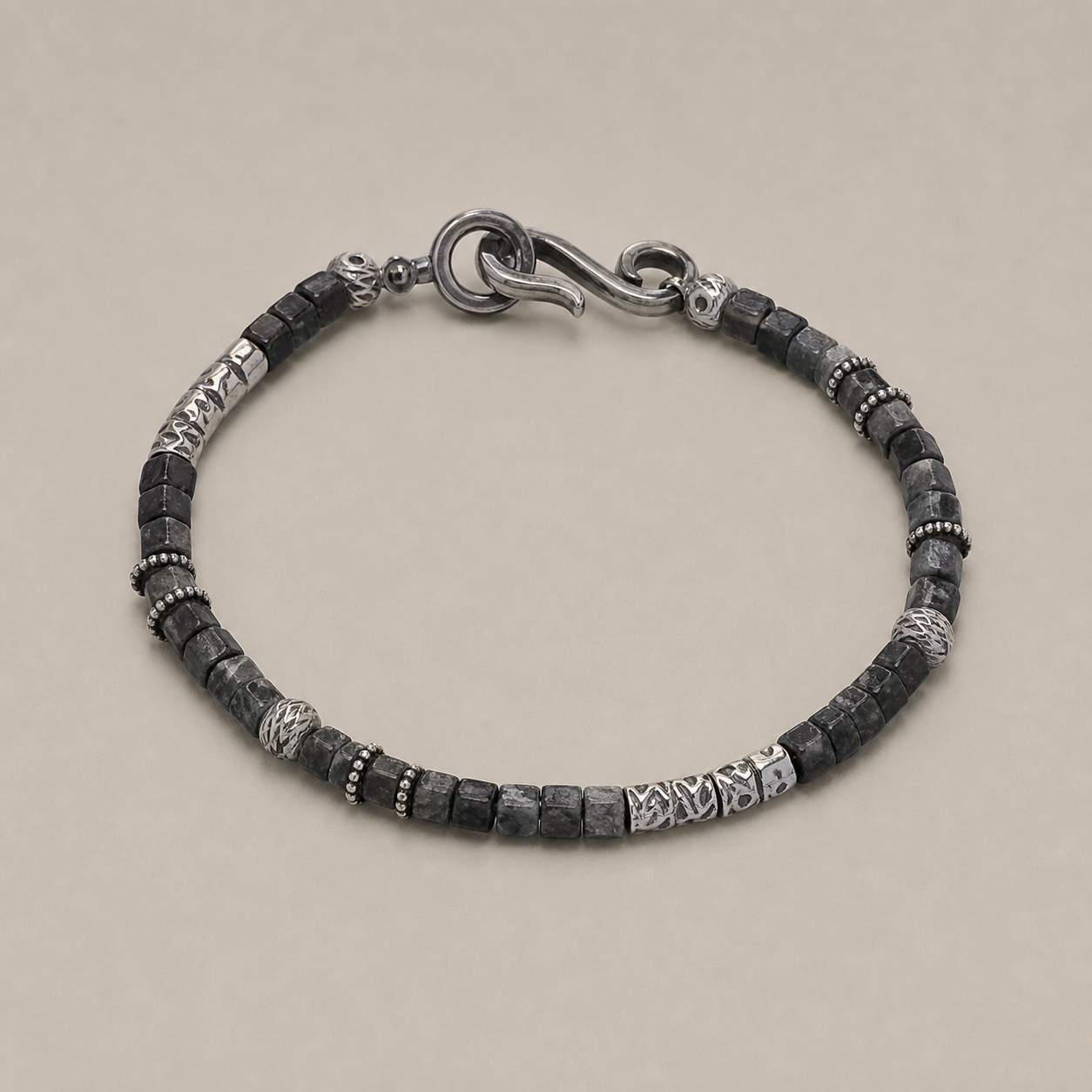 Black-gray beaded bracelet arranged on a warm stone-gray background